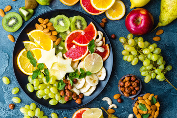 Healthy vegetarian bowl dish with fresh fruits and nuts. Plate with raw apple, orange, grapefruit, banana, kiwi, lemon, grape, almond, hazelnut and cashew nuts. Healthy balanced eating