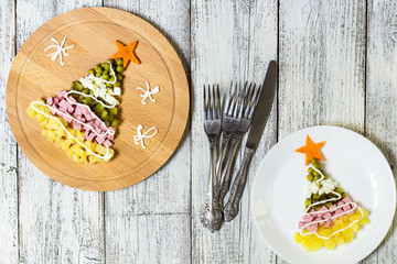 Christmas tree from a salad olivier in plate on a white wooden table. Top view with a copy space