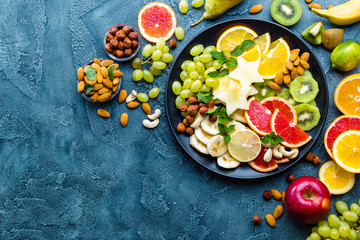 Obraz na płótnie Canvas Healthy vegetarian bowl dish with fresh fruits and nuts. Plate with raw apple, orange, grapefruit, banana, kiwi, lemon, grape, almond, hazelnut and cashew nuts. Healthy balanced eating