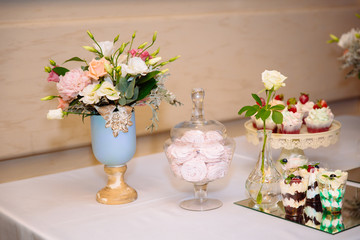 Candy bar, a table with sweets and desserts on the table. Buffet with delicious cupcakes, cake pops, biscuits, flowers.