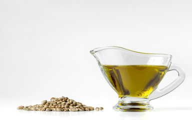 Hemp oil iin a glass gravy boat with a bunch of canabis seeds. Isolated on white background.