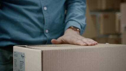 Close-up Shot of Professional Warehouse Worker Checks and Seales Cardboard Box Ready for Shipment. In the Background  Rows of Shelves with Cardboard Boxes with Ready Orders. - Powered by Adobe
