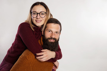Portrait of happy young couple embracing each other in warm knitted sweaters. Happy, funny couple hugging attractive woman and handsome bearded man isolated on grey