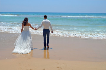 Long-haired brunette bride and groom in a suit. newlyweds holding hands, go to the sand in the water of the Indian Ocean. Wedding and honeymoon in the tropics on the island of Sri Lanka