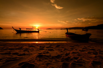 Red sunset on a beach with silouhette of boats in Thailand
