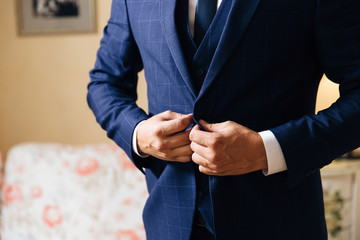 Close-up of a cropped frame of a business stylish man buttoning his jacket, standing in a stylish office with designer repair.