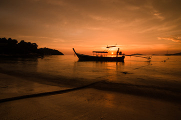 Red sunset on a beach with silouhette of a boat in Thailand
