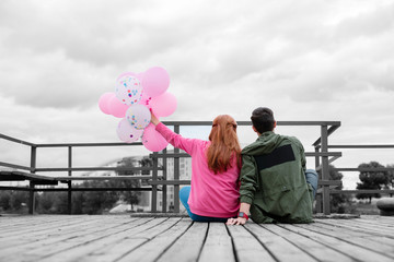 Backs of couple. Young romantic couple having unusual date on the pier and long haired girl holding balloons