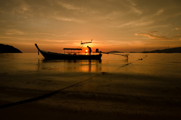 Fototapeta na wymiar Red sunset on a beach with silouhette of a boat in Thailand