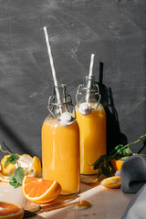 still life, orange juice in glass bottles on a wooden table in the rays of the sun with sliced slices and sprigs of mint