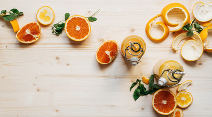 top view, still life, orange juice in glass bottles on a wooden table with orange slices and peel and sprigs of mint flatlay