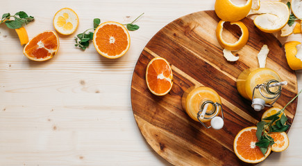 top view, still life, orange juice in glass bottles on a dark wooden plate on a bright wooden table with orange slices and sprigs of mint