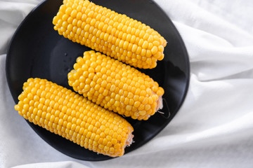 fresh boiled corn of golden color on a black plate on a white background top view