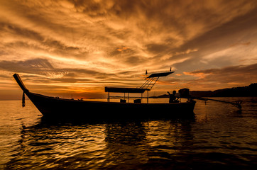 Red sunset on a beach with silouhette of a boat in Thailand