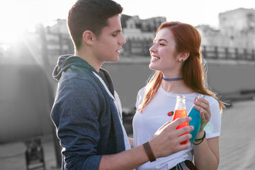 Delicious drinks. Cheerful young couple looking at each other and talking while enjoying delicious colorful cocktails in glass bottles