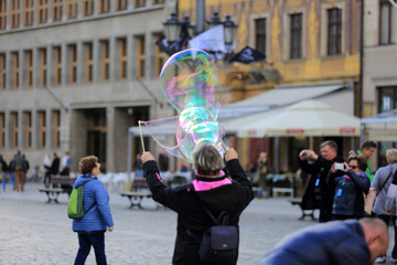 Kobieta puszcza ogromną bańkę mydlaną na rynku Wrocławia.