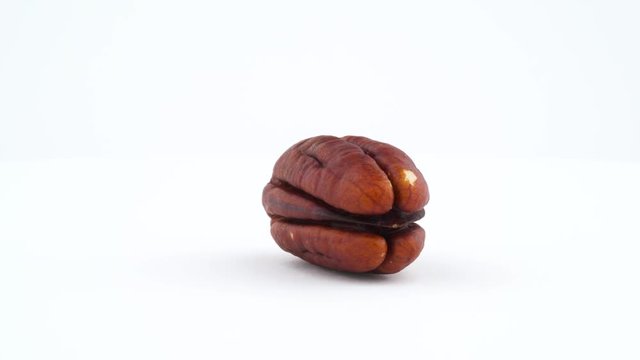 One blanched pecan nut. Rotating on the turntable isolated on the white background. Close up. Macro.