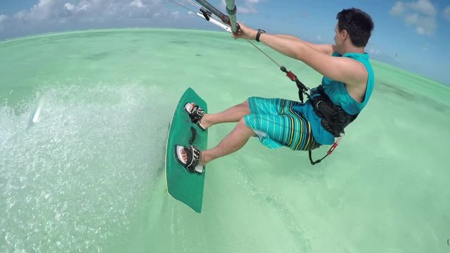 Loop of CLOSE UP: Cheerful young kiteboarder kiting in perfect blue lagoon on Zanzibar