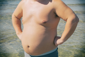 A fat man in shorts stands on the shore of the sea