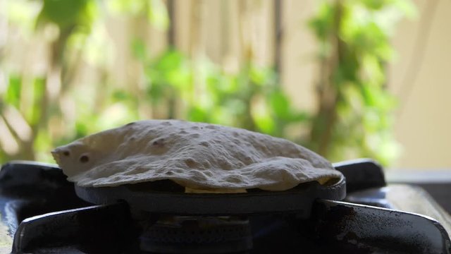 footage of making of Phulka a kind of Chapati: Indian thin bread made from wheat dough being baked on gas stove in home.
