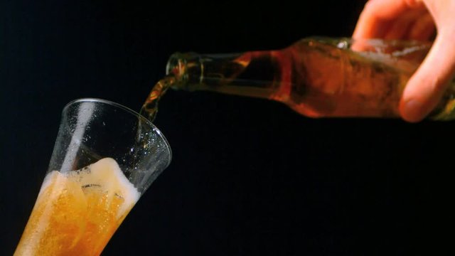 Loop of Hand pouring bottle of beer into glass on black background