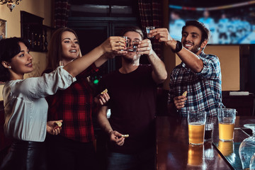 Group of happy multiracial friends making a toast with vodka while standing at bar or pub.