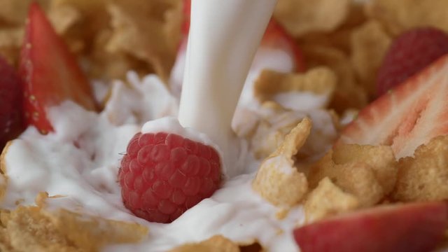 Loop of Corn flakes with raspberry and strawberry in a bowl pouring with milk. Shot with high speed camera, phantom flex 4K. Slow Motion.