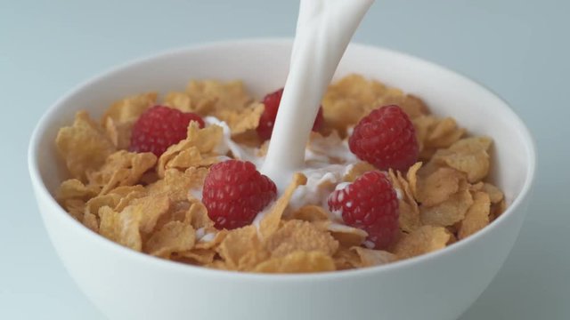 Loop of Corn flakes with raspberry in a bowl pouring with milk. Shot with high speed camera, phantom flex 4K. Slow Motion.