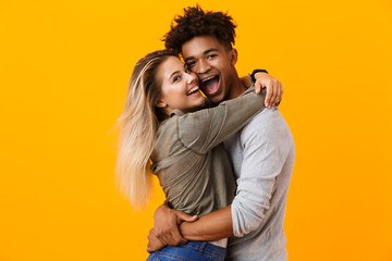 Cute young loving couple posing isolated over yellow background hugging.