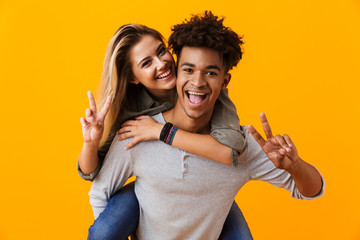 Happy cute young loving couple posing isolated over yellow background hugging showing peace gesture.
