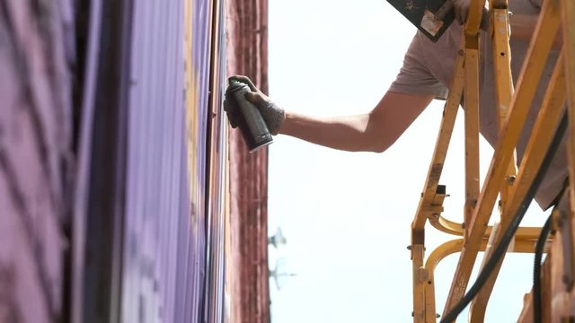 A low view: A young male artist draws a can of graffiti paint on a wall. It should be on a construction tower. A man engaged in art
