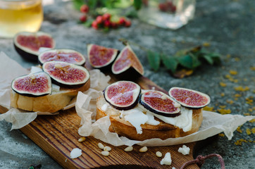 Bruschetta with cheese, fresh figs, pine nuts and honey on rustic board