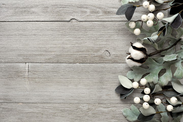 Side border of silver green leaves and white berries over a rustic gray wood background. Top view...