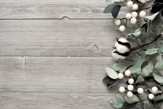 Side border of silver green leaves and white berries over a rustic gray wood background. Top view with copy space.