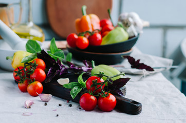  Cutting board surrounded by fresh raw tomato, sweet pepper, basil, olive oil and spice on the table