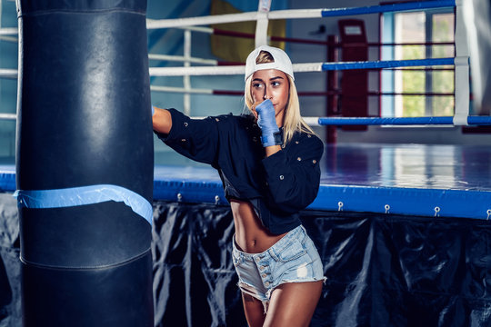 Concentrated blonde woman doing a fitness boxing workout with a punching bag. The girl in the boxing hall emotionally beats the boxing bag