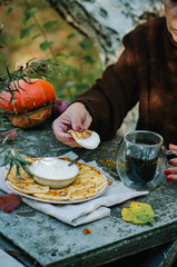 Autumn breakfast with pancakes. Cottage cheese pancakes кussian syrniki with sour cream. A woman in a brown sweater is drinking coffee.
