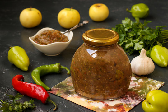 Homemade sauce adjika with hot pepper, garlic, apples, parsley and dill in a jar on a dark background