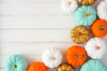 Autumn corner border of various colorful pumpkins on a white wood background. Top view with copy...