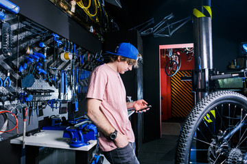 A young, stylish redheaded male small business owner selling and repairing a bike is wearing a blue...