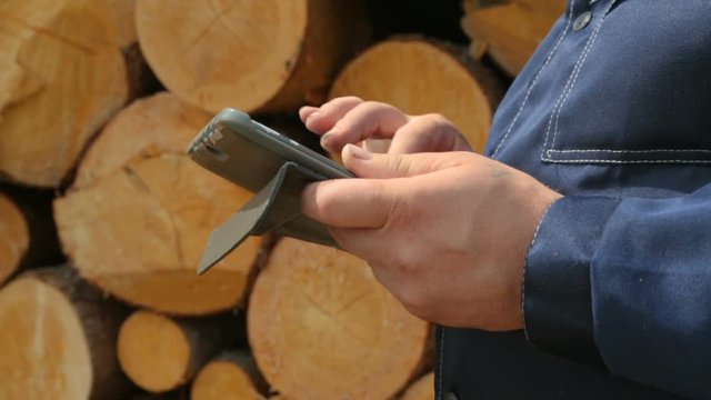 Worker with tablet PC against pile of logs