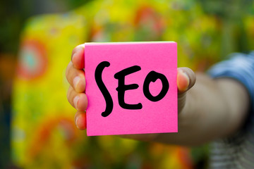 Hand holding an pink Paper with word SEO, Business Concept. colourful background
