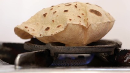 footage of making of Phulka a kind of Chapati: Indian thin bread made from wheat dough being baked on gas stove in home.