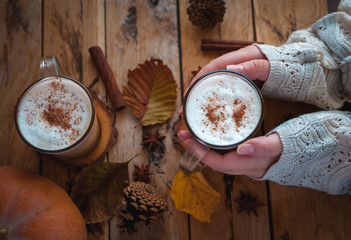 Hands holding pumpkin spice latte in glass cup on wooden background 