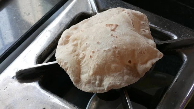 footage of making of Phulka a kind of Chapati: Indian thin bread made from wheat dough being baked on gas stove in home.