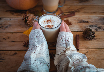 Hands holding pumpkin spice latte in glass cup on wooden background 