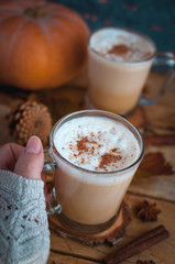 Close-up of hand holding pumpkin spice latte in glass cup on wooden background 