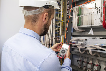 Young adult electrician builder engineer inspecting electric equipment in distribution fuse box....