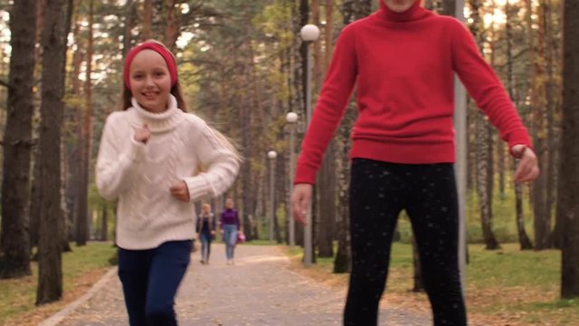 Young happy girls running on road in autumn park together in slow motion