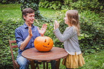 Happy halloween. Father and daughter playing with a pumpkin outside.